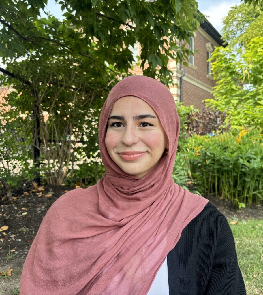 A photo of a person wearing a pink hijab outside surrounded by greenery.