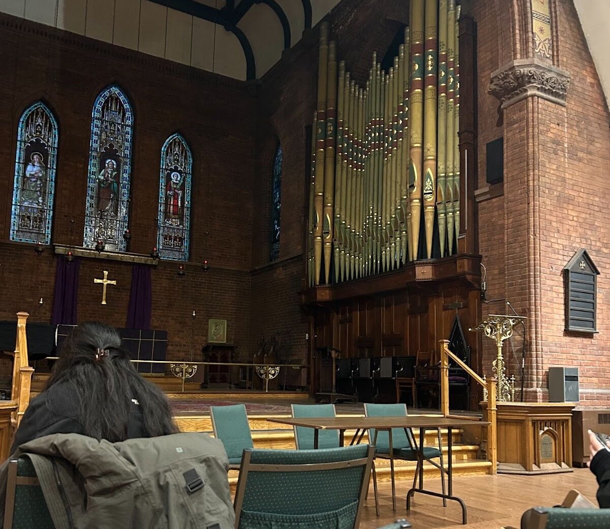 People seated in chairs inside a church, with a large pipe organ visible in the background